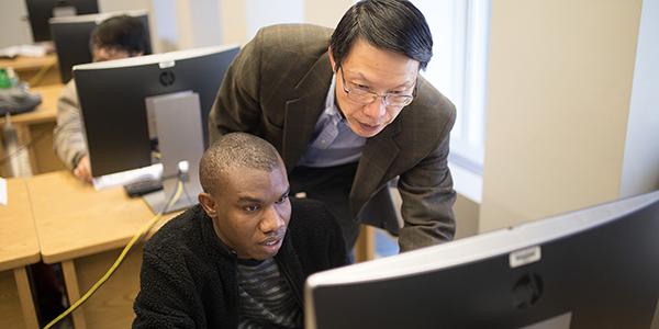 student in front of computer with professor standing behind him